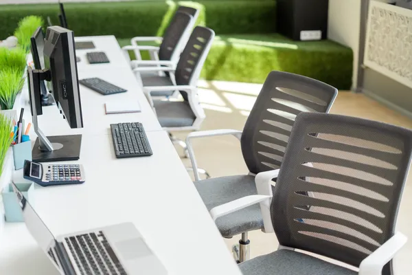 Varios escritorios blancos, que están equipados con unas computadoras y unas sillas de oficina negro con blanco