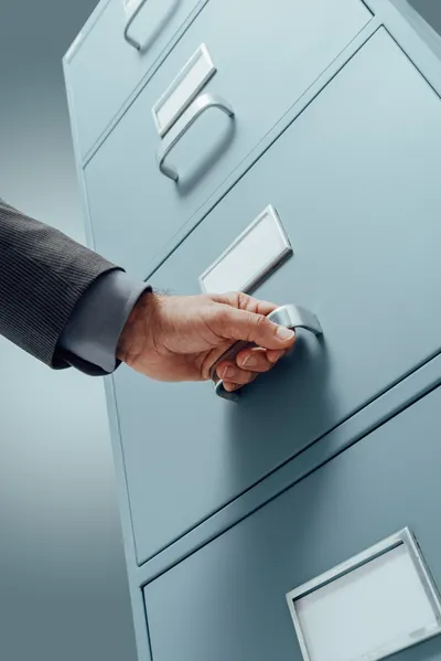 Una mano abriendo un archivero para oficina, es amplio y está acomodado de manera vertical, es metalico